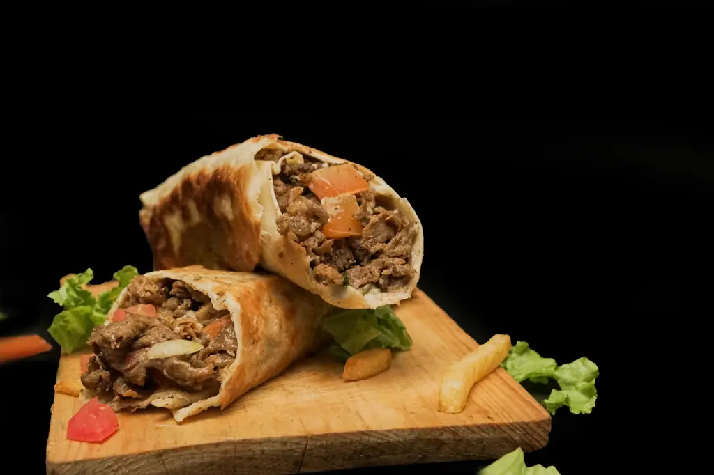 Zwei Hälften eines gefüllten Wraps mit Fleisch und Salat auf einem Holzbrett