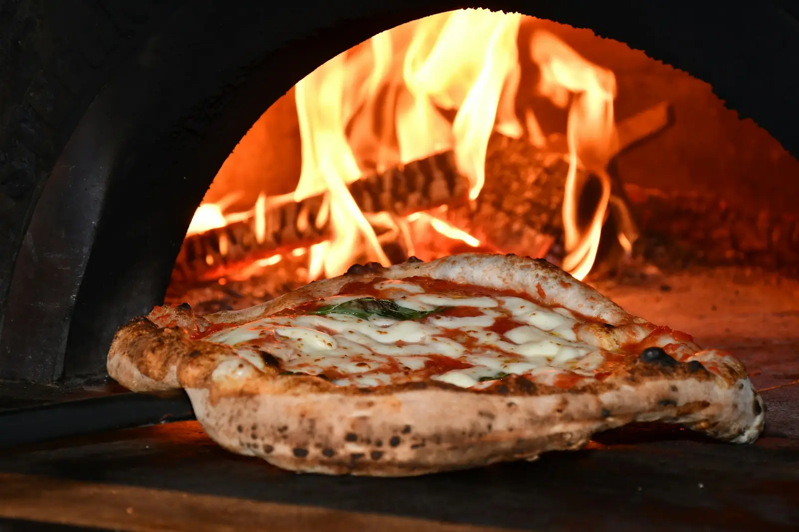 Pizza Margherita backt im Holzofen vor offenem Feuer