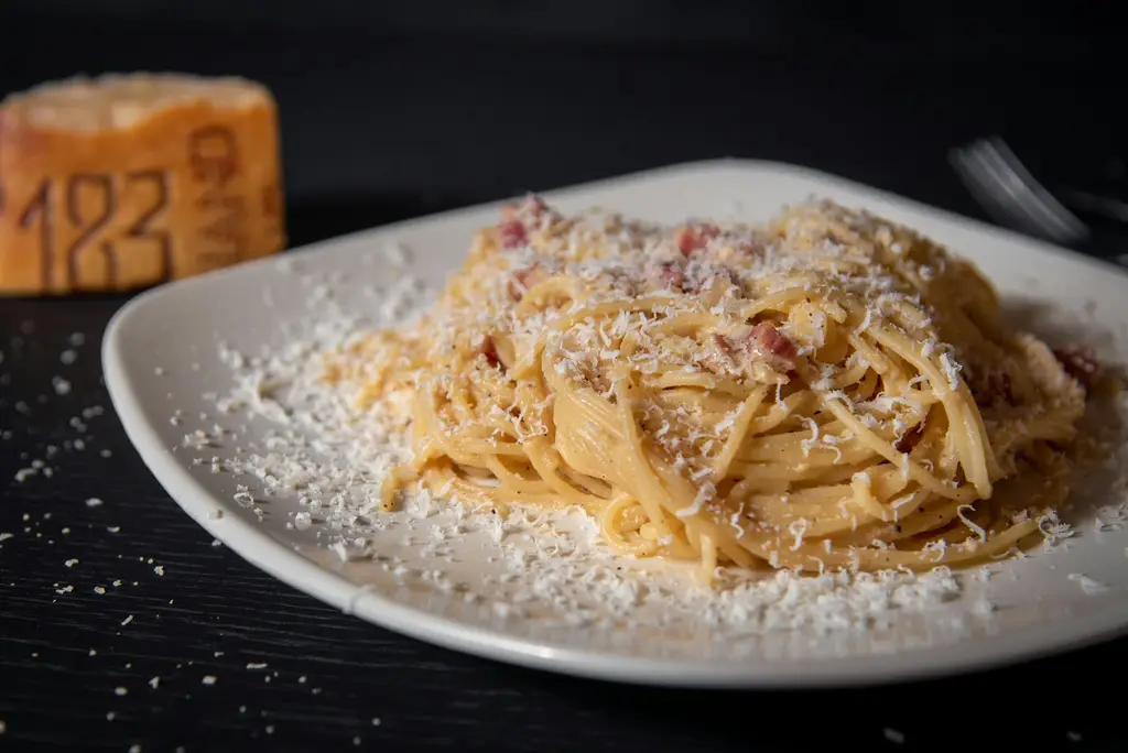 Spaghetti in cremiger Sauce mit frisch geriebenem Käse auf einem weißen Teller