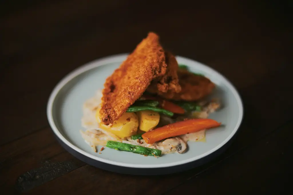 Knusprig paniertes Schnitzel mit Gemüse auf einem dunklen Teller