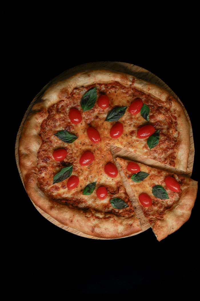 High-angle view of a Margherita pizza with cherry tomatoes and basil on a wooden board.