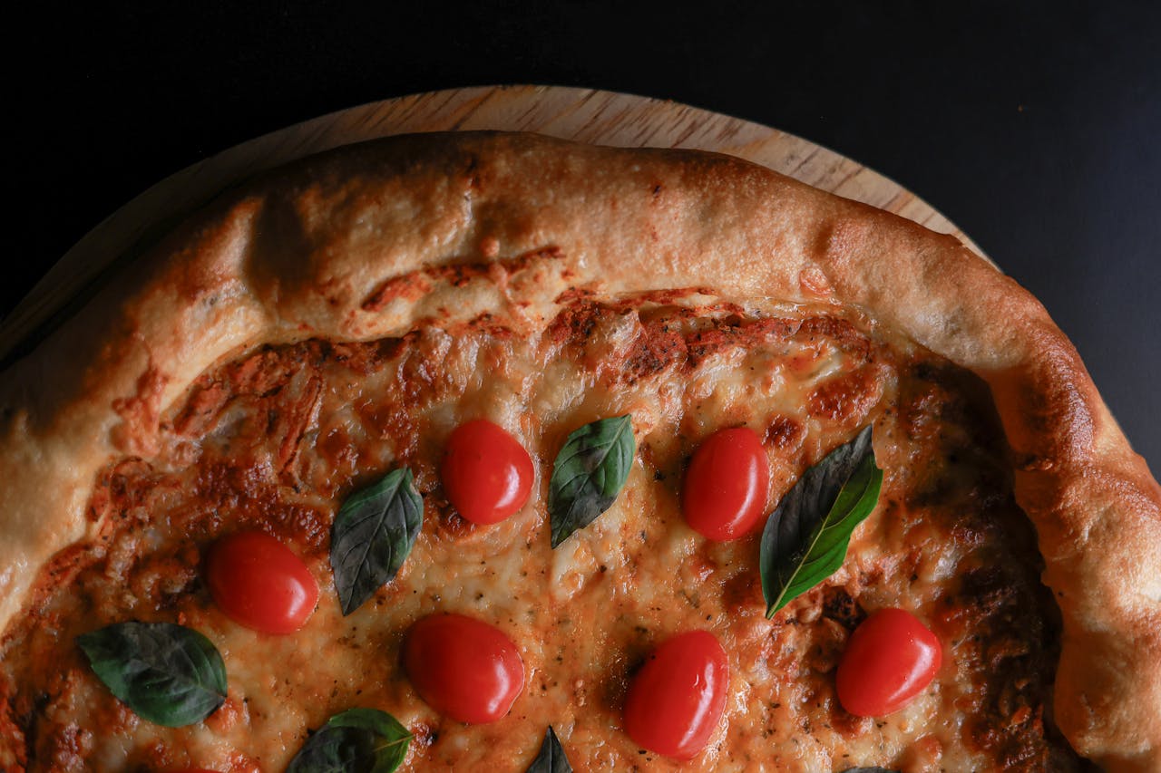 Close-up of a Margherita pizza with cherry tomatoes and basil on a wooden board.